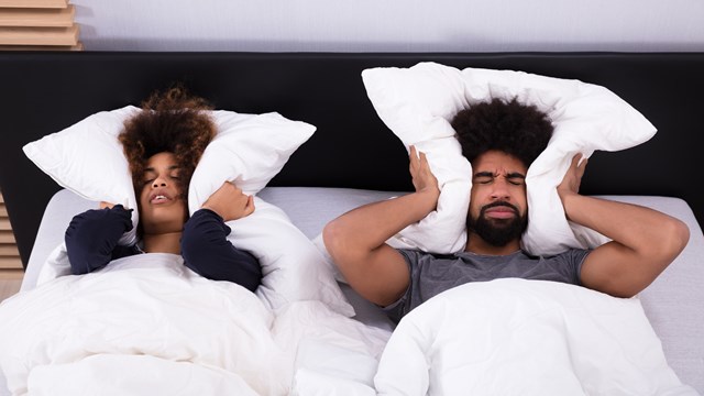 Elevated View Of Young Couple Lying In Bed Covering Their Ears With Pillow