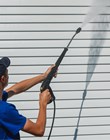 Worker in overalls washes a white wall from a siding with a water gun. Cleaning service for washing buildings and facades