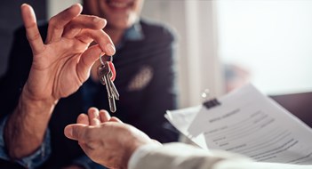 Q&A: Defining ‘Owner-Occupied’ Real estate agent sitting at the desk by the window and passing keys to his client in the office