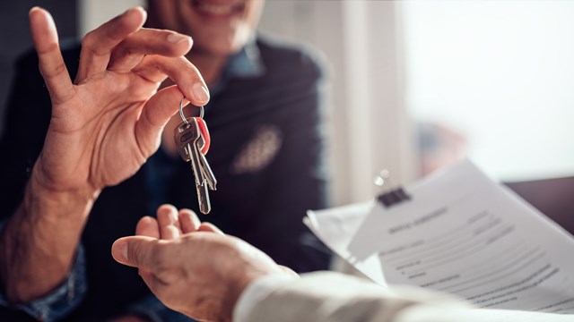 Real estate agent sitting at the desk by the window and passing keys to his client in the office