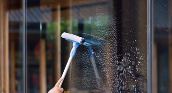 Clear Benefits to Clean Windows A person is cleaning a window with a squeegee. The window is covered in streaks and the person is using a blue and white squeegee to clean it