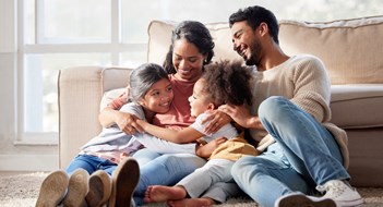 Families, Kids, & Quiet Enjoyment Affectionate and loving mixed race family sitting together. Happy family with two daughters hugging their mother and bonding at home. Two little girls enjoying a happy childhood with mom and dad