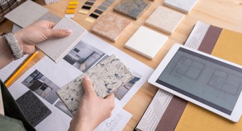 Working With Designers Hands of young female designer holding two samples of marble tile over wooden table with digital tablet, photos of home interior etc