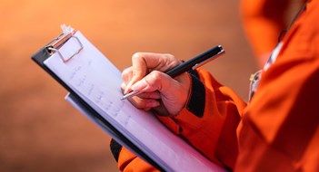 Self-Managed  Communities vs. Local Laws & Regulations Safety officer/Supervisor is writing note on the checklist paper during perform audit and inspection in oil field operation. Close-up action and selective focus photo.