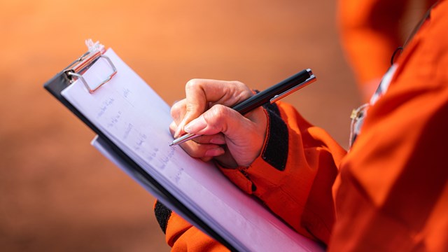 Safety officer/Supervisor is writing note on the checklist paper during perform audit and inspection in oil field operation. Close-up action and selective focus photo.