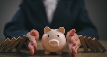 Protecting Your Reserves Businesswoman placed a wooden block on a piggy bank. stop the domino crisis effect, financial and banking problems, recession, financial crisis, bad debt, inflation and interest rates, asset safety