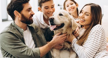 Families, Kids & Quality of Life Family sitting together on a sofa in their living room, joyfully hugging their beloved golden retriever. Parents and children sharing laughter and playful moments, embodying love and togetherness