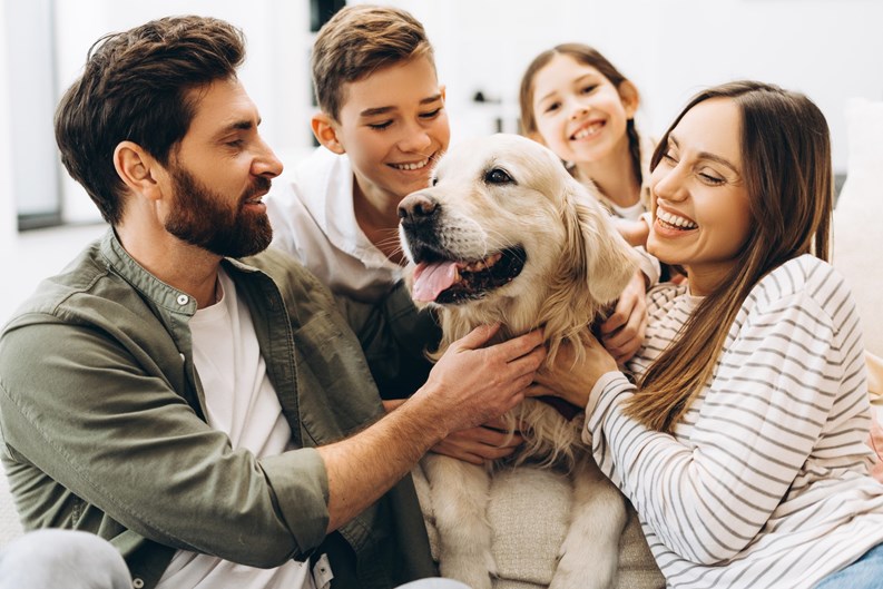 Family sitting together on a sofa in their living room, joyfully hugging their beloved golden retriever. Parents and children sharing laughter and playful moments, embodying love and togetherness