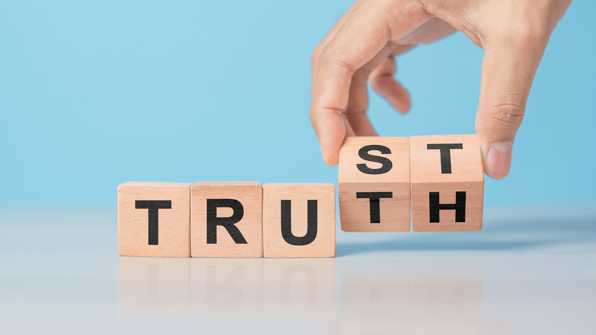 Hand flipping wooden cube with TRUST and TRUTH words. Concept of business ethics, honesty, integrity, and building trustworthy relationships. Clean table background