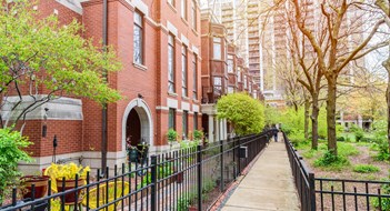 Navigating Chicago’s Façade Ordinance Modern brick row houses with bay windows along a fenced paved path on the side of a public park. A high rise block of flats is in background. Chicago, IL, USA.