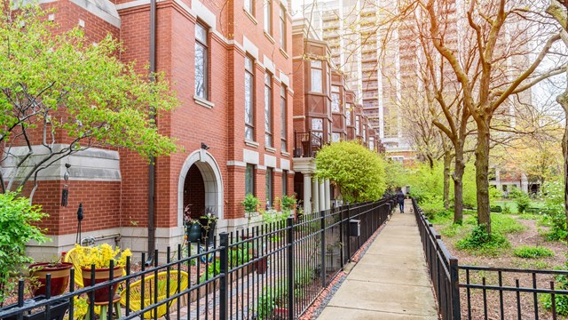 Modern brick row houses with bay windows along a fenced paved path on the side of a public park. A high rise block of flats is in background. Chicago, IL, USA.