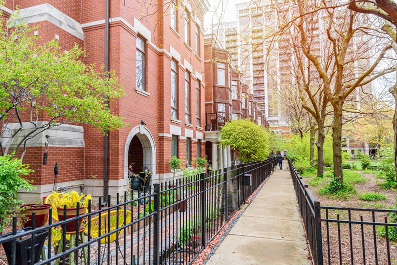 Modern brick row houses with bay windows along a fenced paved path on the side of a public park. A high rise block of flats is in background. Chicago, IL, USA.