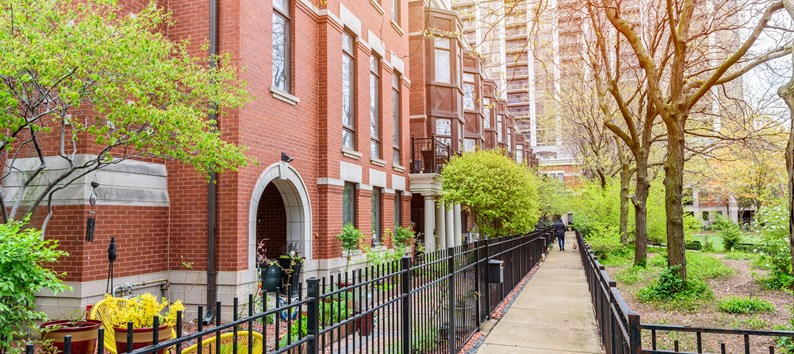 Modern brick row houses with bay windows along a fenced paved path on the side of a public park. A high rise block of flats is in background. Chicago, IL, USA.