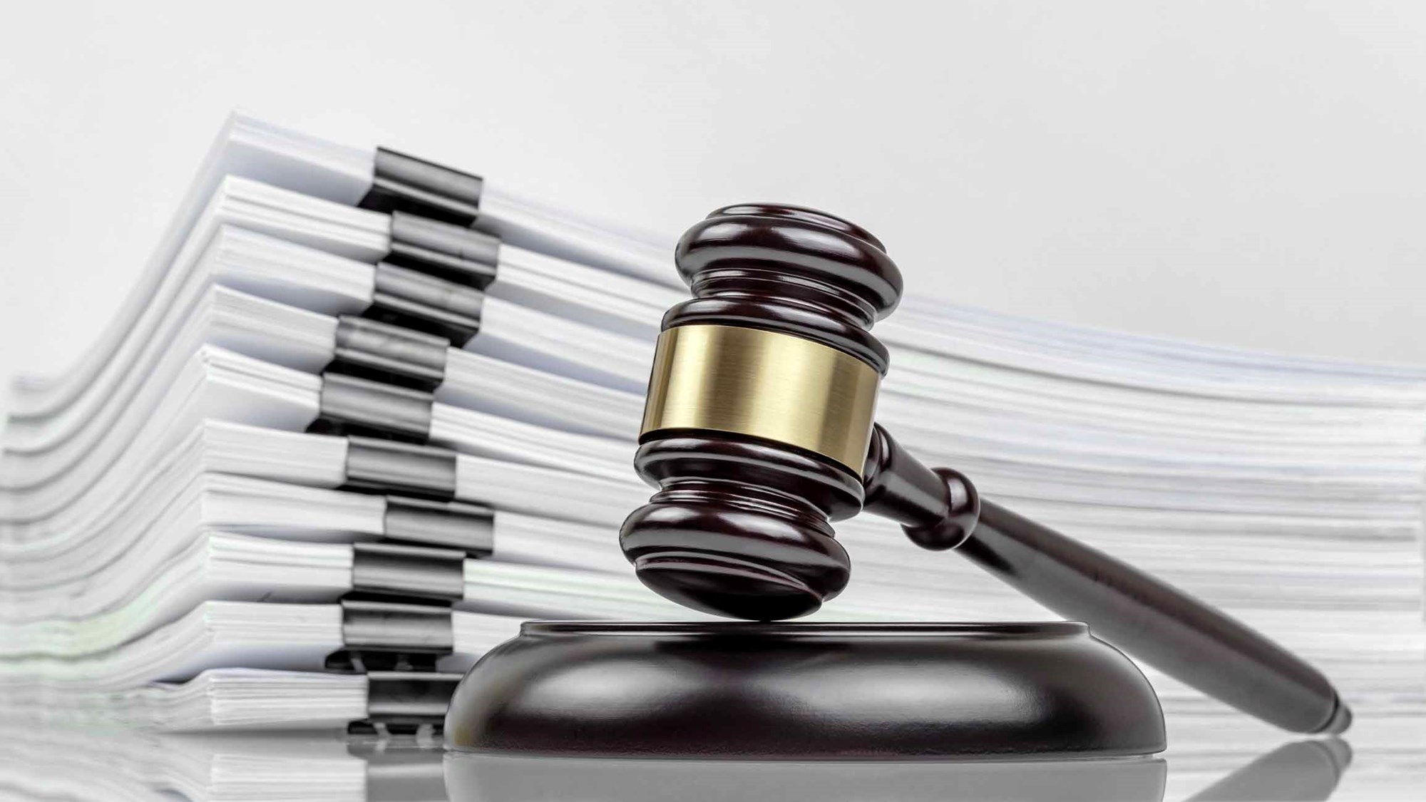 Close-up of a judge's gavel and a stack of court files and documents on a desk. Judicial case backlogs and accumulation.