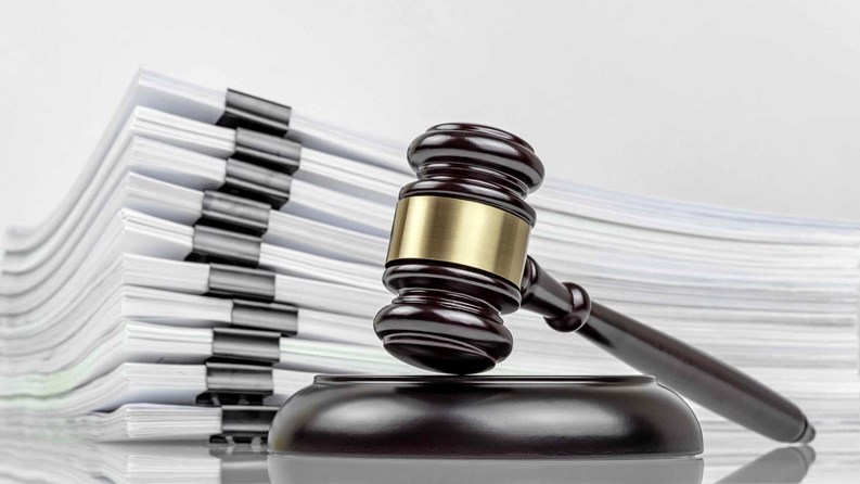 Close-up of a judge's gavel and a stack of court files and documents on a desk. Judicial case backlogs and accumulation.